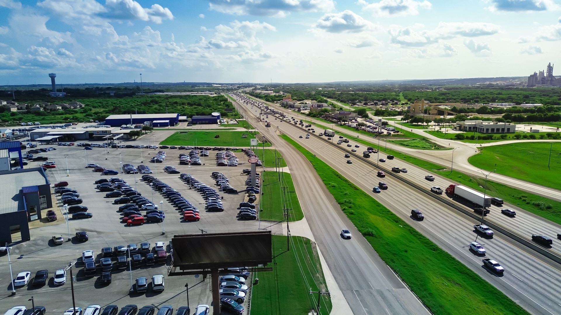 Blank highway billboard of car dealership near Interstate highway I-35 frontage road in New Braunfels, suburbs San Antonio, Texas, wide variety of auto brands display at parking lot, aerial view