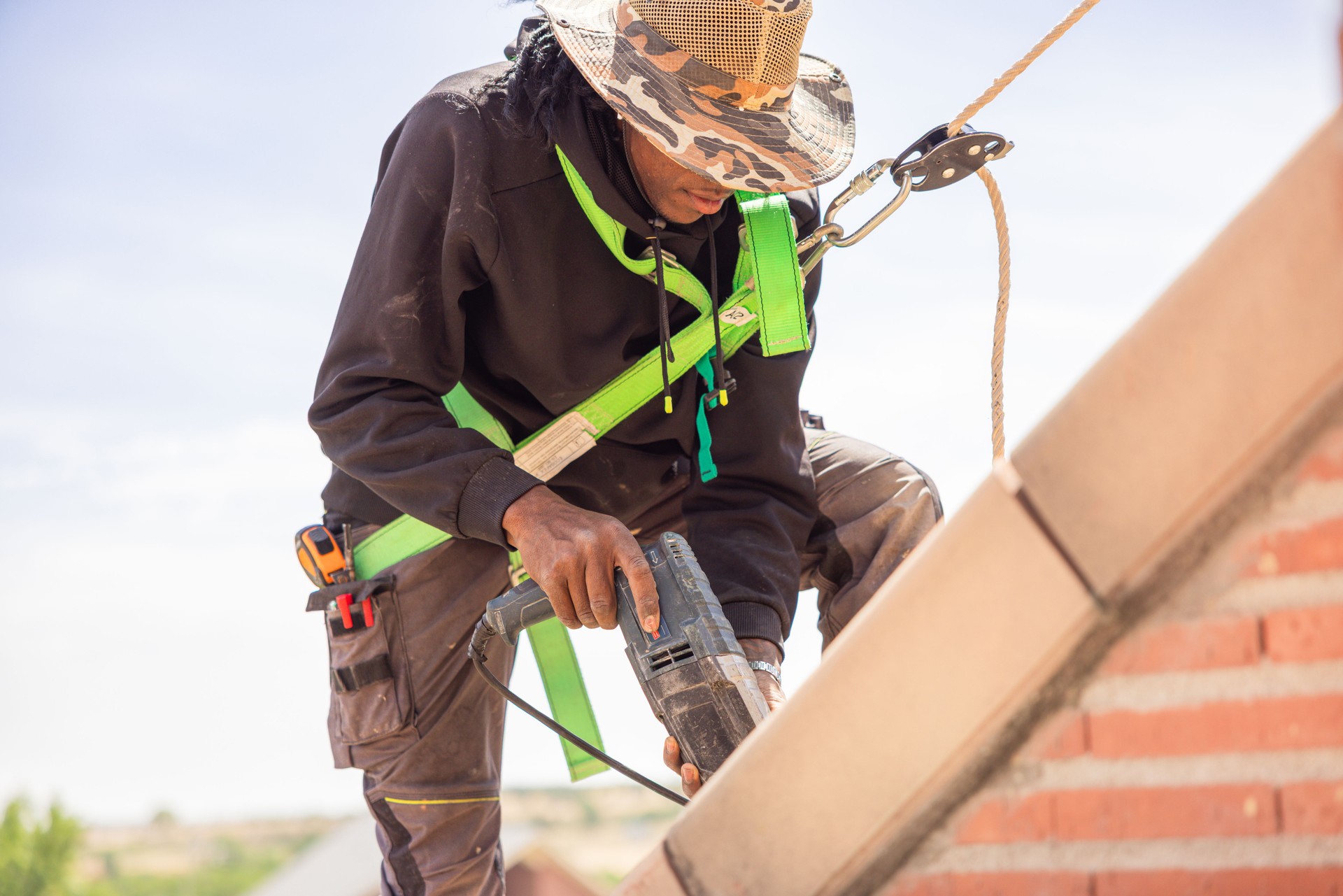 Young african american worker installing tiles with electric drill wearing safety harness